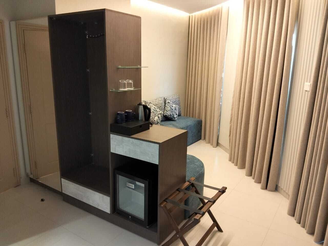 Una habitación compacta con armario, pequeño kitchenette, sofá y ventana cubierta por cortinas.