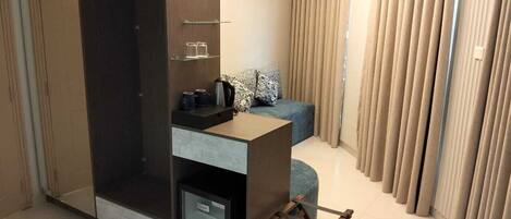 Una habitación compacta con armario, pequeño kitchenette, sofá y ventana cubierta por cortinas.