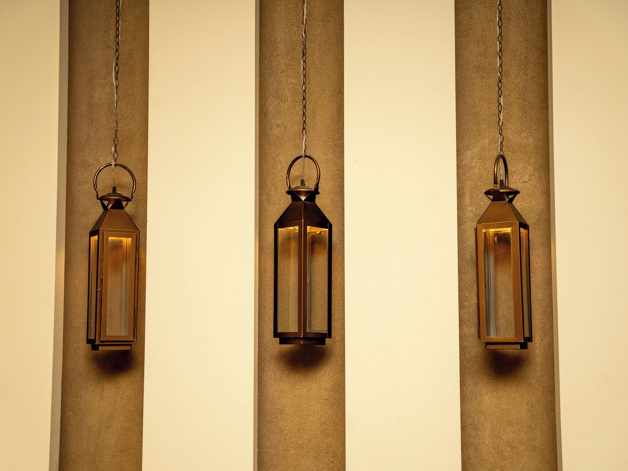 Three hanging lantern-style lights against a textured wall.