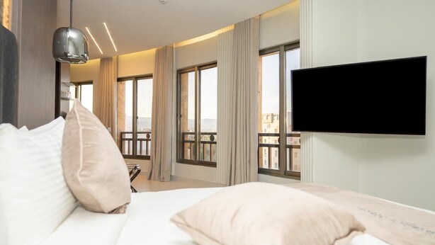 A hotel room with a large bed, a flat-screen TV mounted on the wall, and a balcony with a view of the city. - Captain's Hotel (Aqaba)