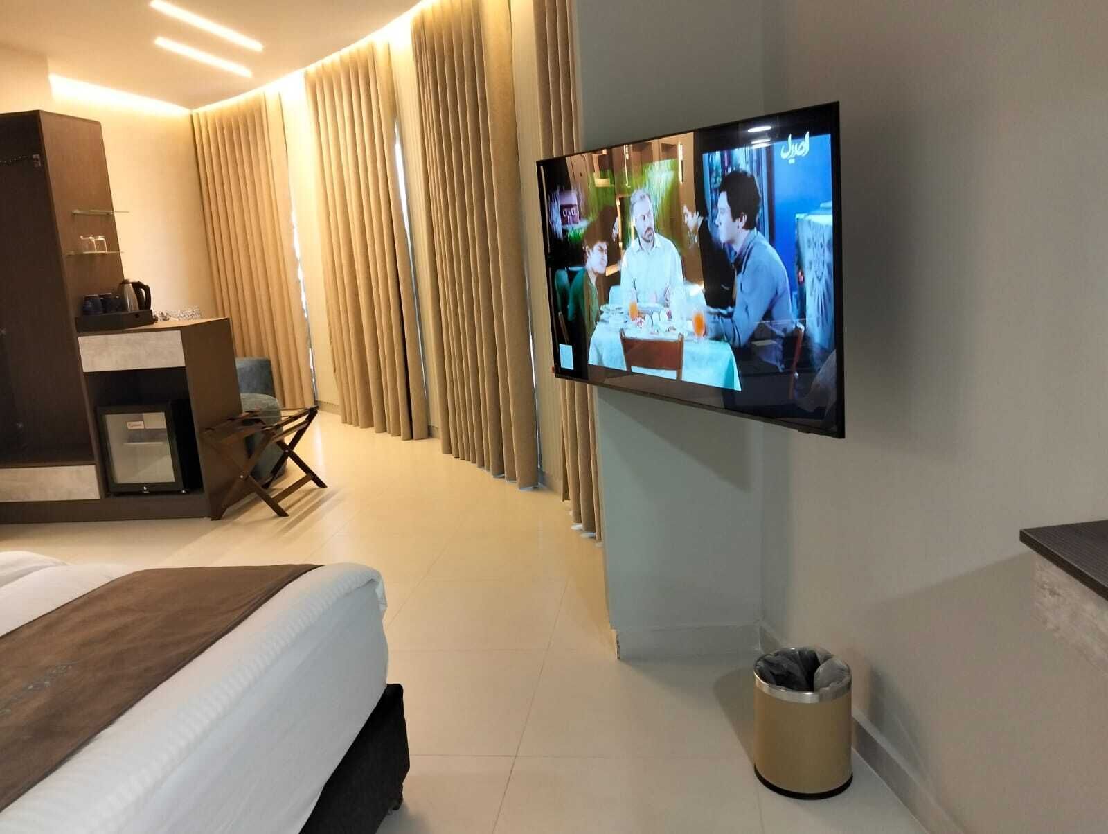 A hotel room with a bed, a TV mounted on the wall, a desk with a chair, and a trash bin.