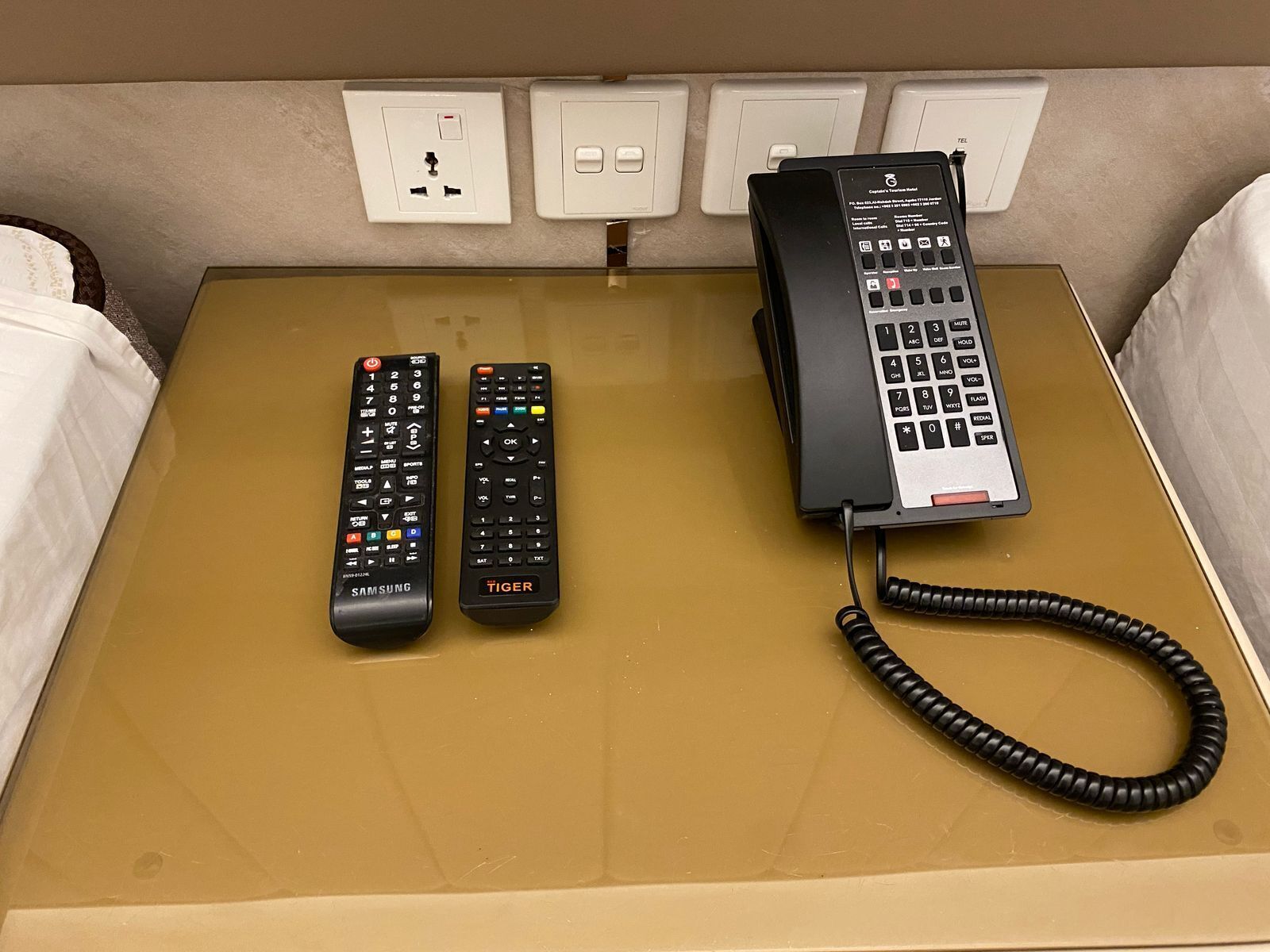 Une chambre d’hôtel avec un lit marron, un téléphone et deux télécommandes posées sur le lit.