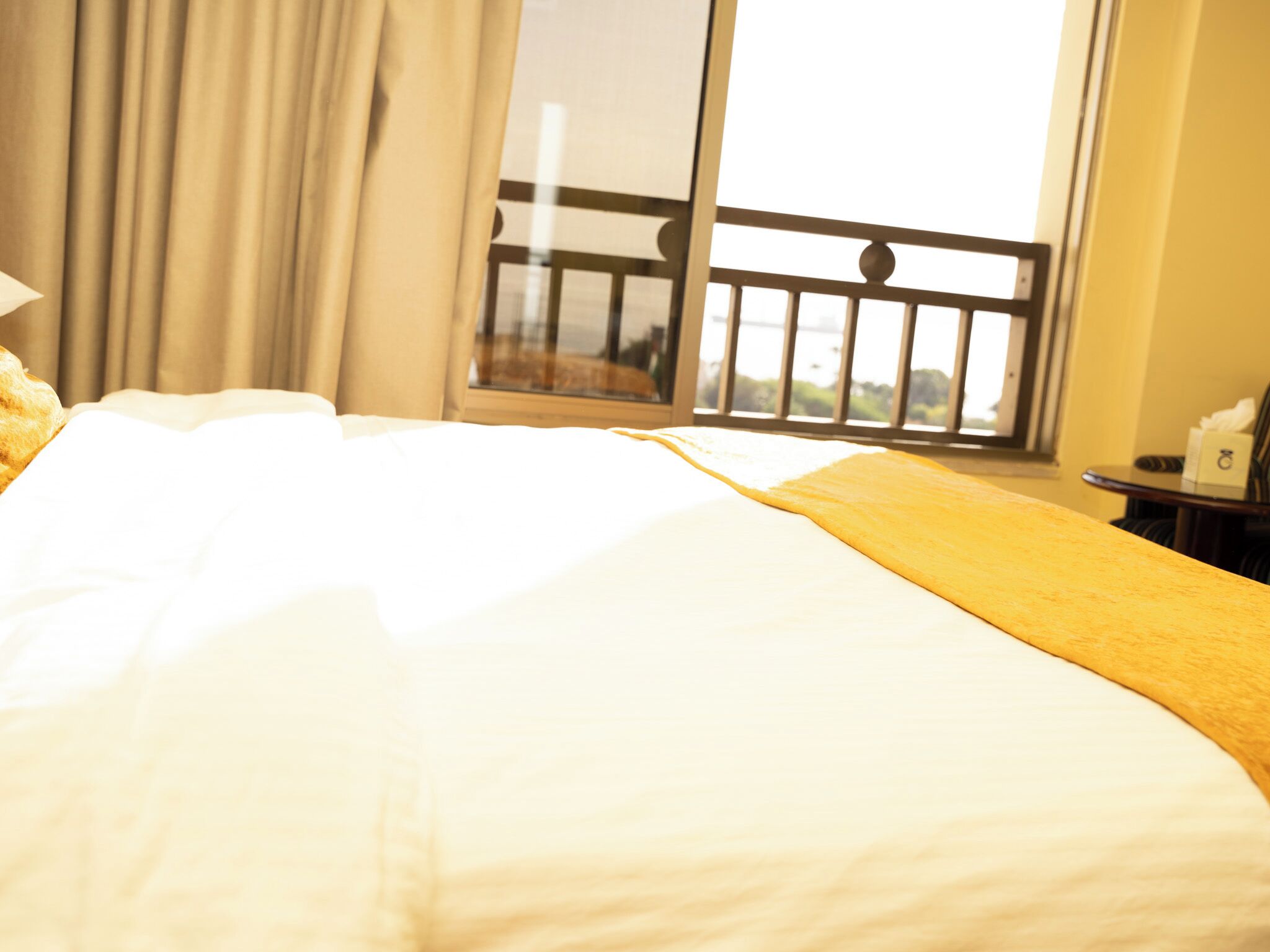 Une chambre d’hôtel avec un grand lit, une fenêtre donnant sur un espace verdoyant et une petite table avec une lampe.