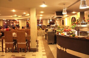 A restaurant with a buffet setup, seating area, and a counter with food items. - Captain's Hotel (Aqaba)