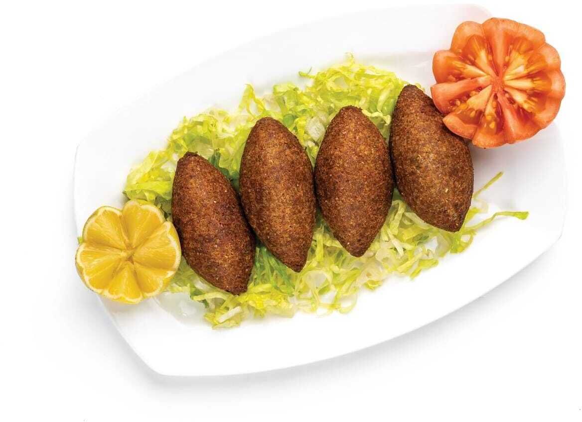 A plate with five falafel balls, a slice of tomato, and a lemon half on a bed of lettuce.