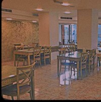 A dining area with wooden tables and chairs, a tiled floor, and a large window with a view.