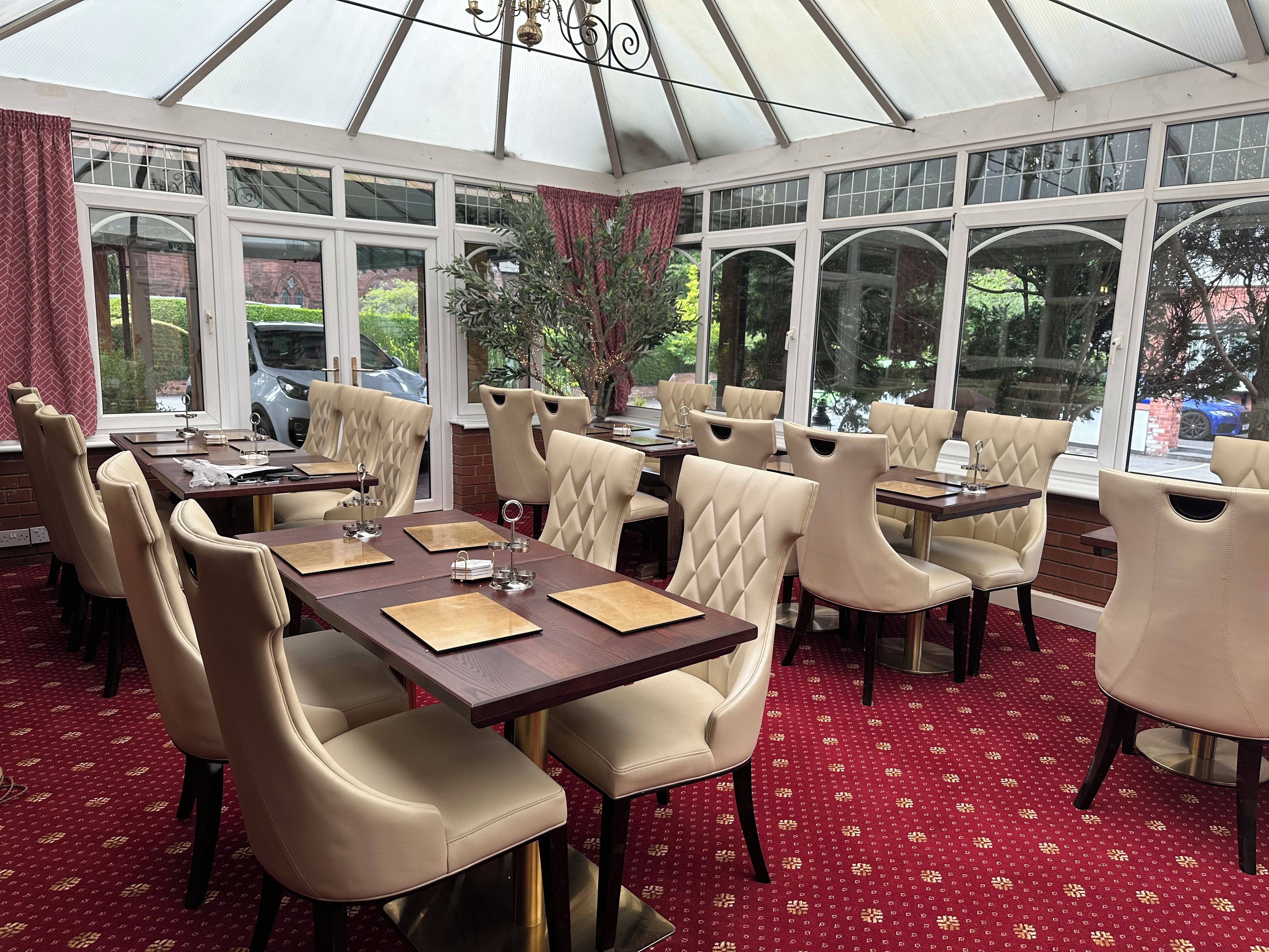 A conservatory with tables and chairs, large windows, and a red patterned carpet.