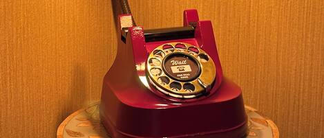 A vintage red rotary dial telephone with a black lamp arm and two exposed bulbs, mounted on a wooden base with a circular design.
