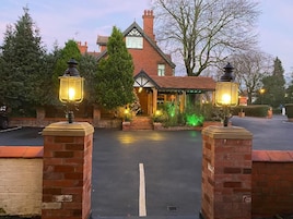 A traditional brick house with a well-lit entrance, a covered porch, and a driveway leading to the front door.