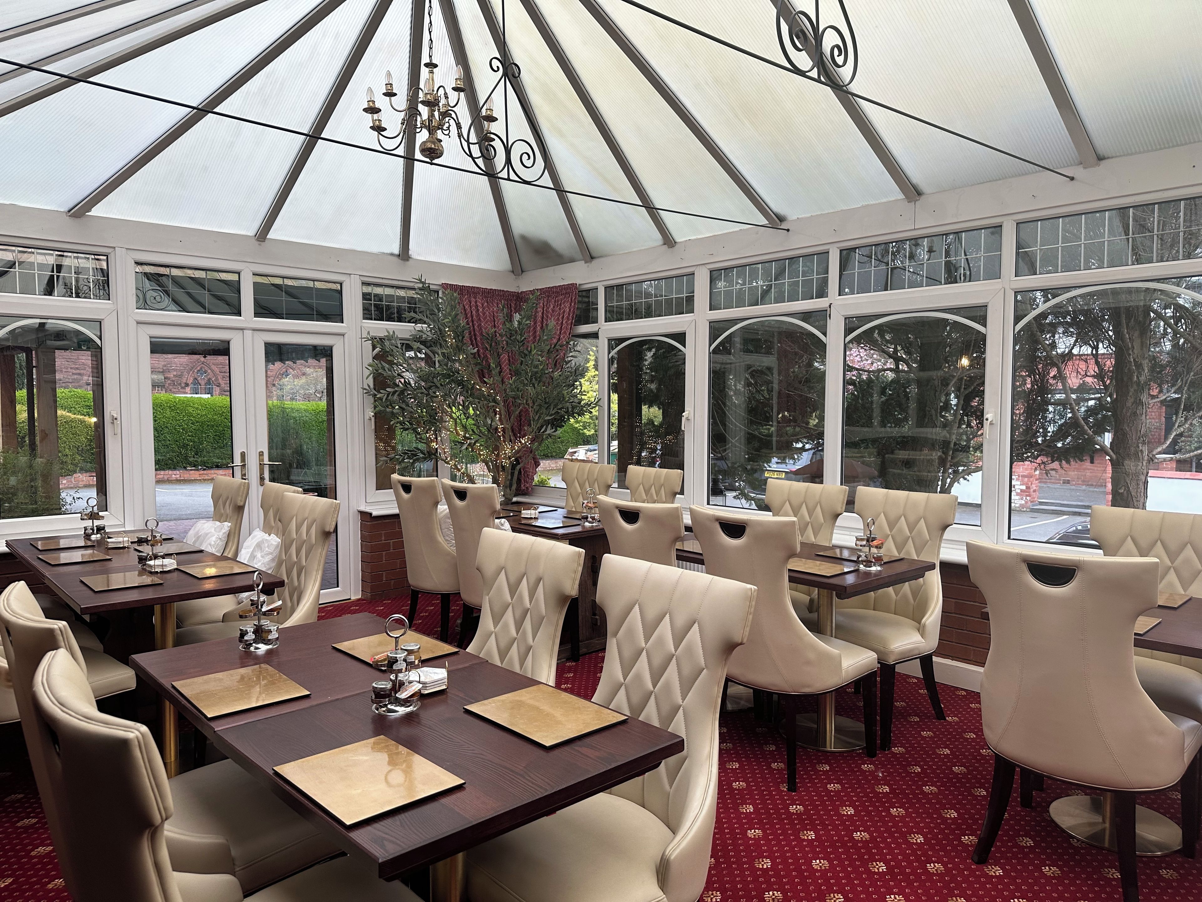 A conservatory with tables and chairs, large windows, and a chandelier.
