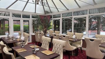 A conservatory with tables and chairs, large windows, and a chandelier.
