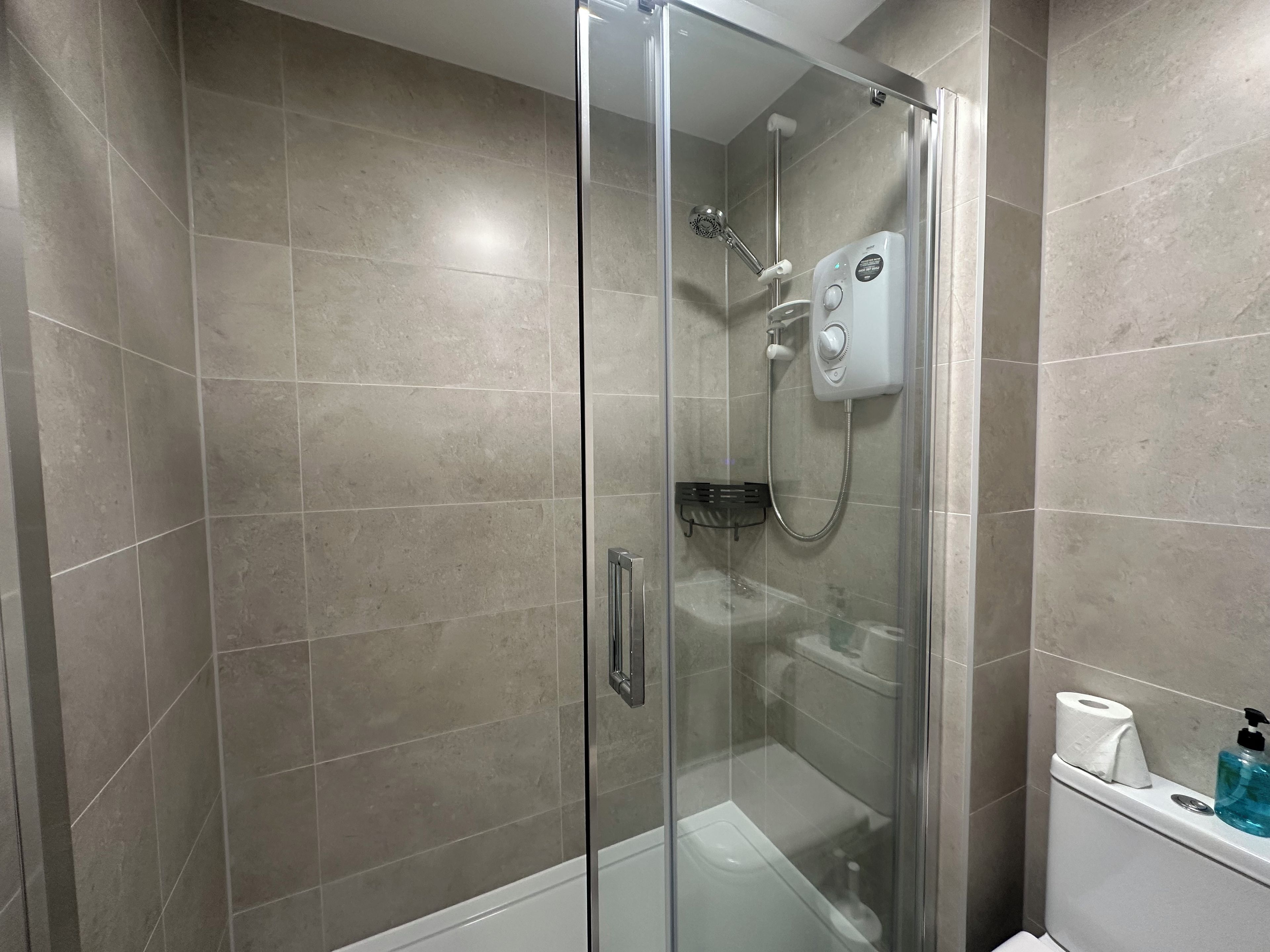 A glass-enclosed shower with a handheld showerhead and a wall-mounted control panel.
