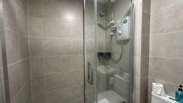 A glass-enclosed shower with a handheld showerhead and a wall-mounted control panel.