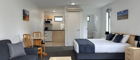 A modern room with a bed, a sofa, a small table, and a kitchenette in the background.