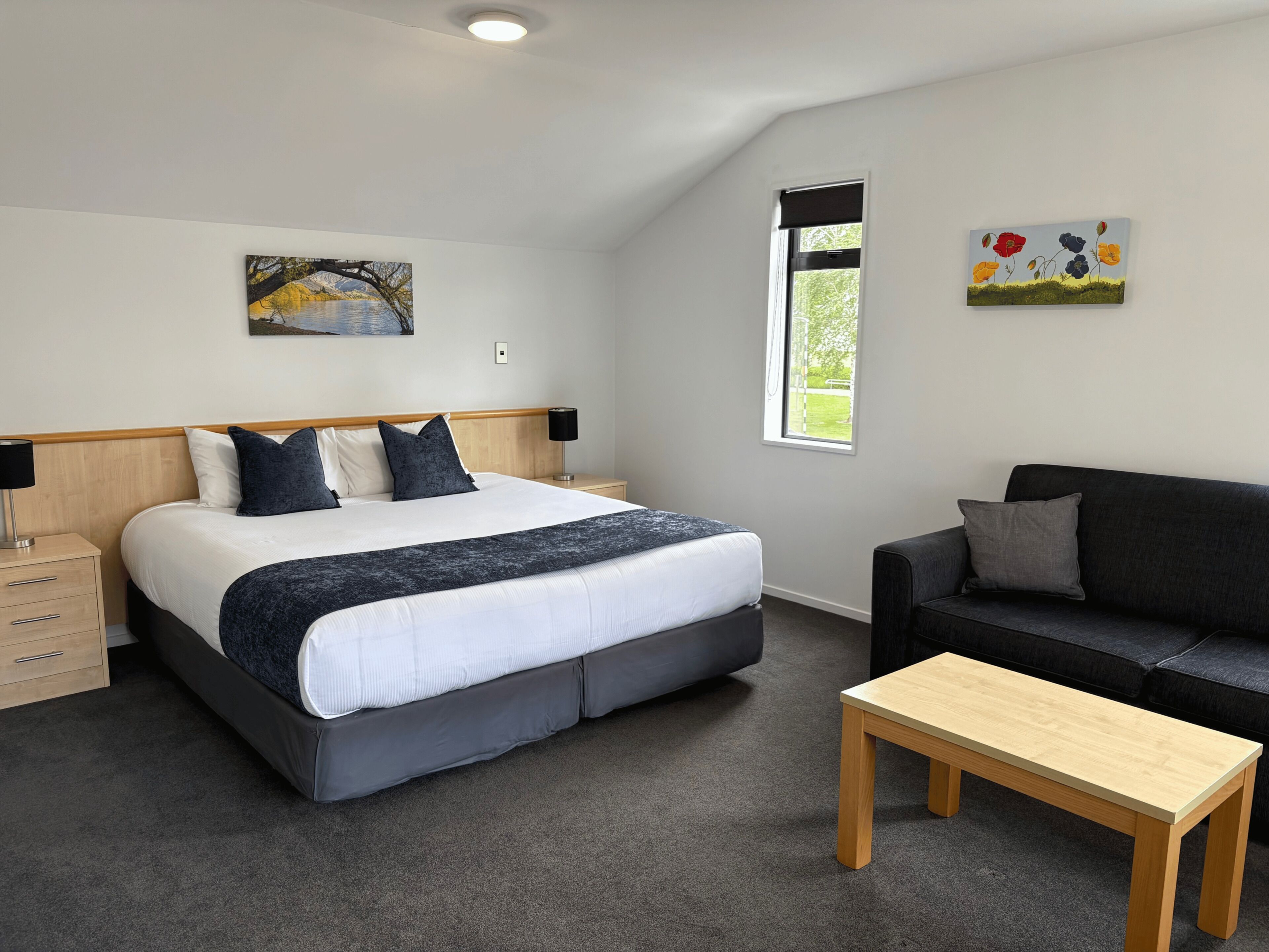 Une chambre à coucher avec un lit, des tables de chevet, une fenêtre, un tableau, un canapé et une table basse.