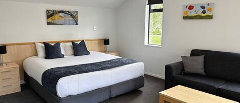 Une chambre à coucher avec un lit, des tables de chevet, une fenêtre, un tableau, un canapé et une table basse.