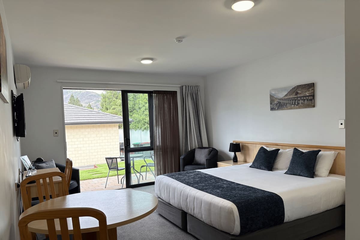 Habitación de hotel con cama, escritorio, sillas, televisor y vistas al exterior.