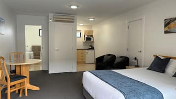 A hotel room with a bed, a desk with two chairs, a kitchenette, and a bathroom.