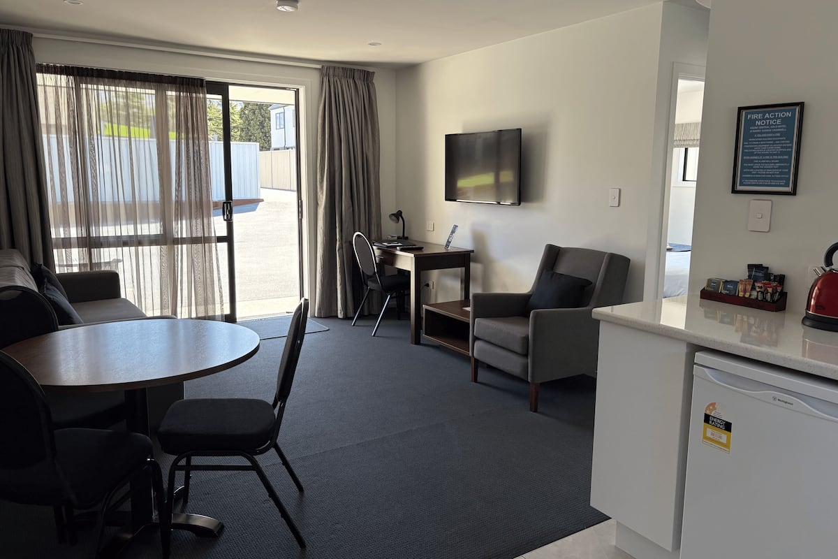 Habitación de hotel con mesa de comedor, sillas, sofá, televisor montado en la pared, escritorio con silla y área de kitchenette.