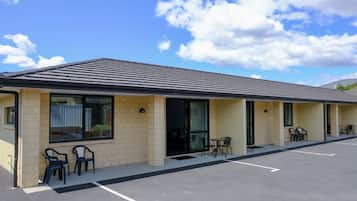 A motel with a row of rooms, each with a door and a window. There are outdoor chairs and tables near the entrance.