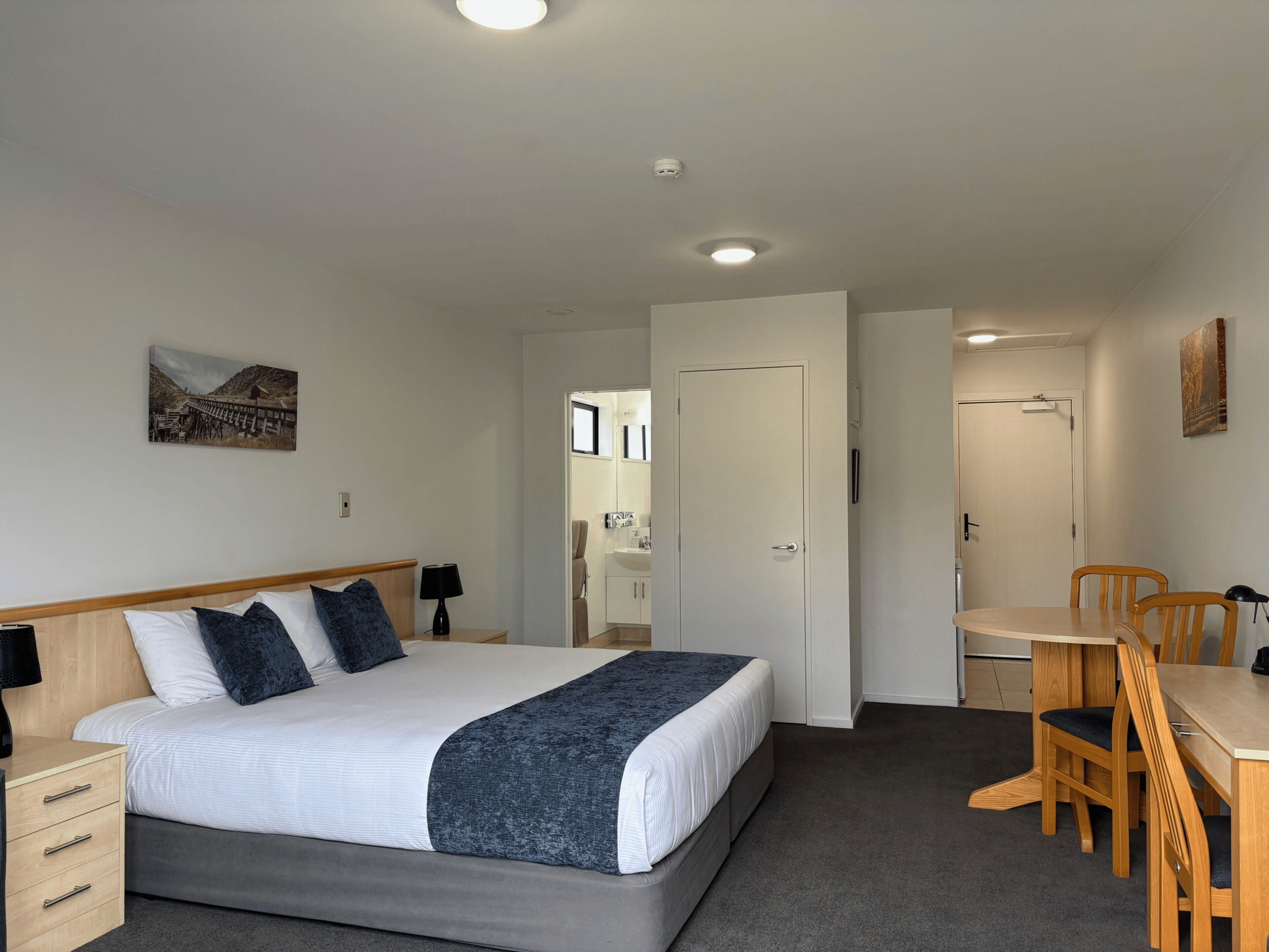 A hotel room with a bed, bedside tables, a desk, and chairs.