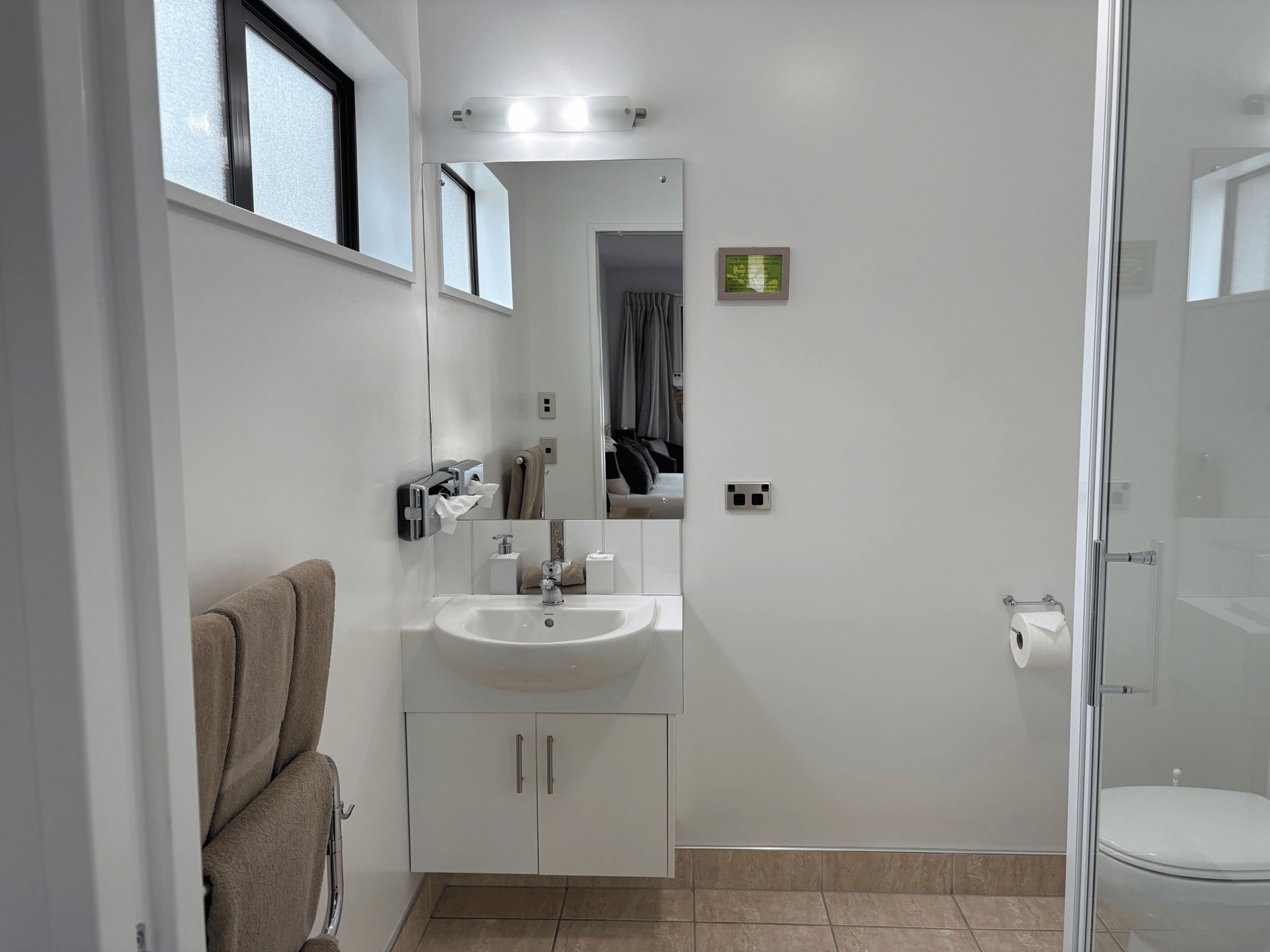 Un baño moderno con lavamanos, espejo, toallero y cabina de ducha de vidrio.