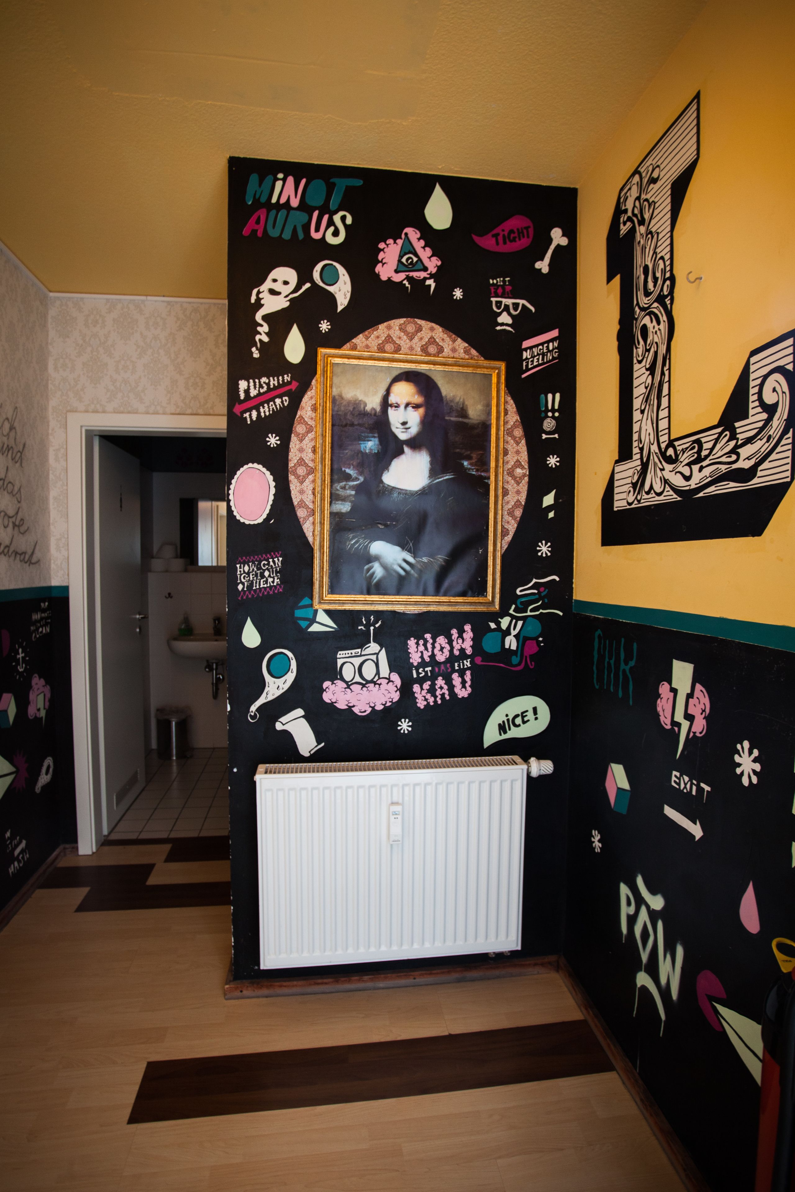 Un pasillo con una pared negra decorada con varias pegatinas y dibujos, incluyendo un cuadro enmarcado de una obra de arte famosa.