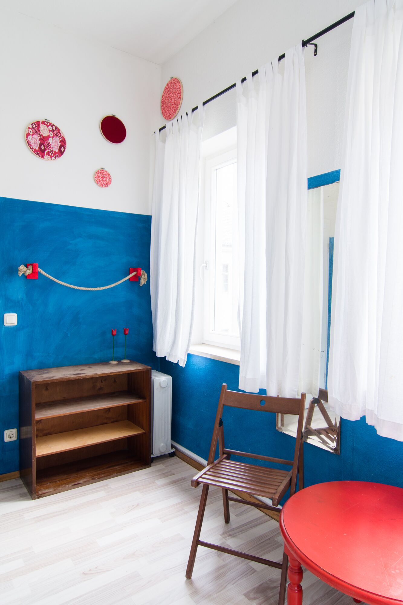 A room with a blue and white color scheme, a wooden chair, a red table, and a window with white curtains.