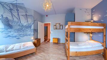 A room with two bunk beds, a wooden desk, a chair, a wall mural of a ship, and a hanging light fixture.
