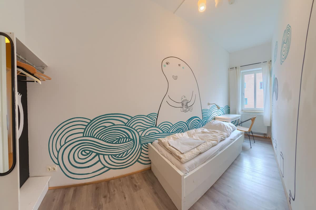A bedroom with a bed, a wall mural, a window, and a wooden floor.