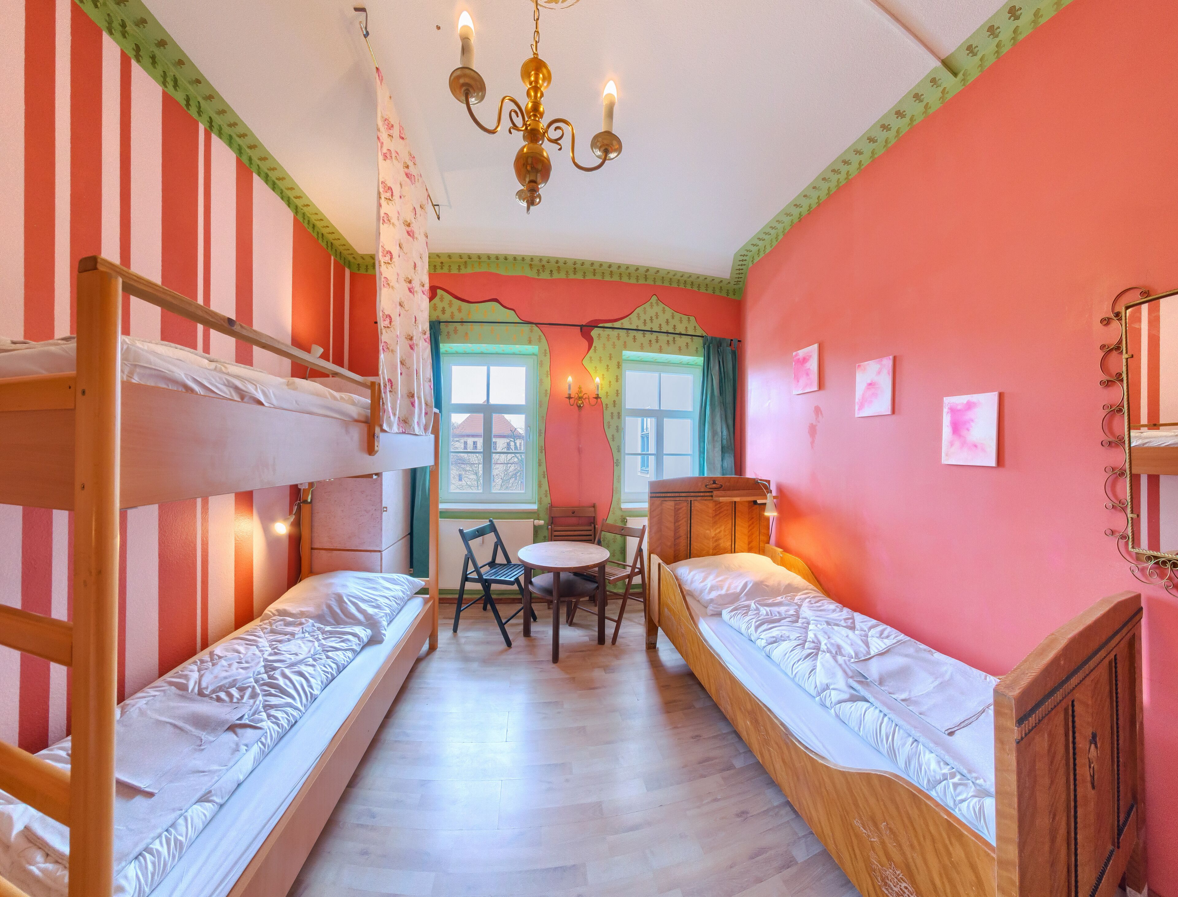 A room with two bunk beds, a table, chairs, a chandelier, and a window with curtains.