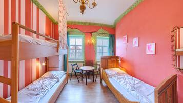 A room with two bunk beds, a table, chairs, a chandelier, and a window with curtains.