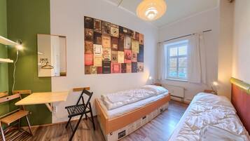 A room with a bunk bed, a desk, a chair, a wall with a collage of vintage book covers, a hanging light fixture, and a window with curtains.