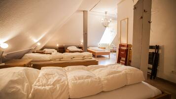 Een ruime kamer onder de dakpannen met een groot bed, een houten bankje en een kleine tafel.