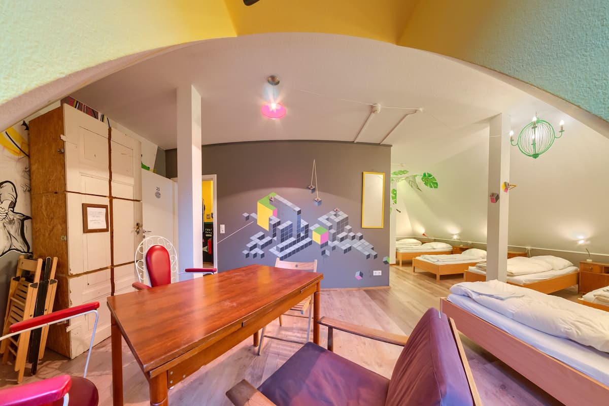 A compact, modern room with a wooden dining table, a red chair, a purple sofa, and a bed with two pillows.
