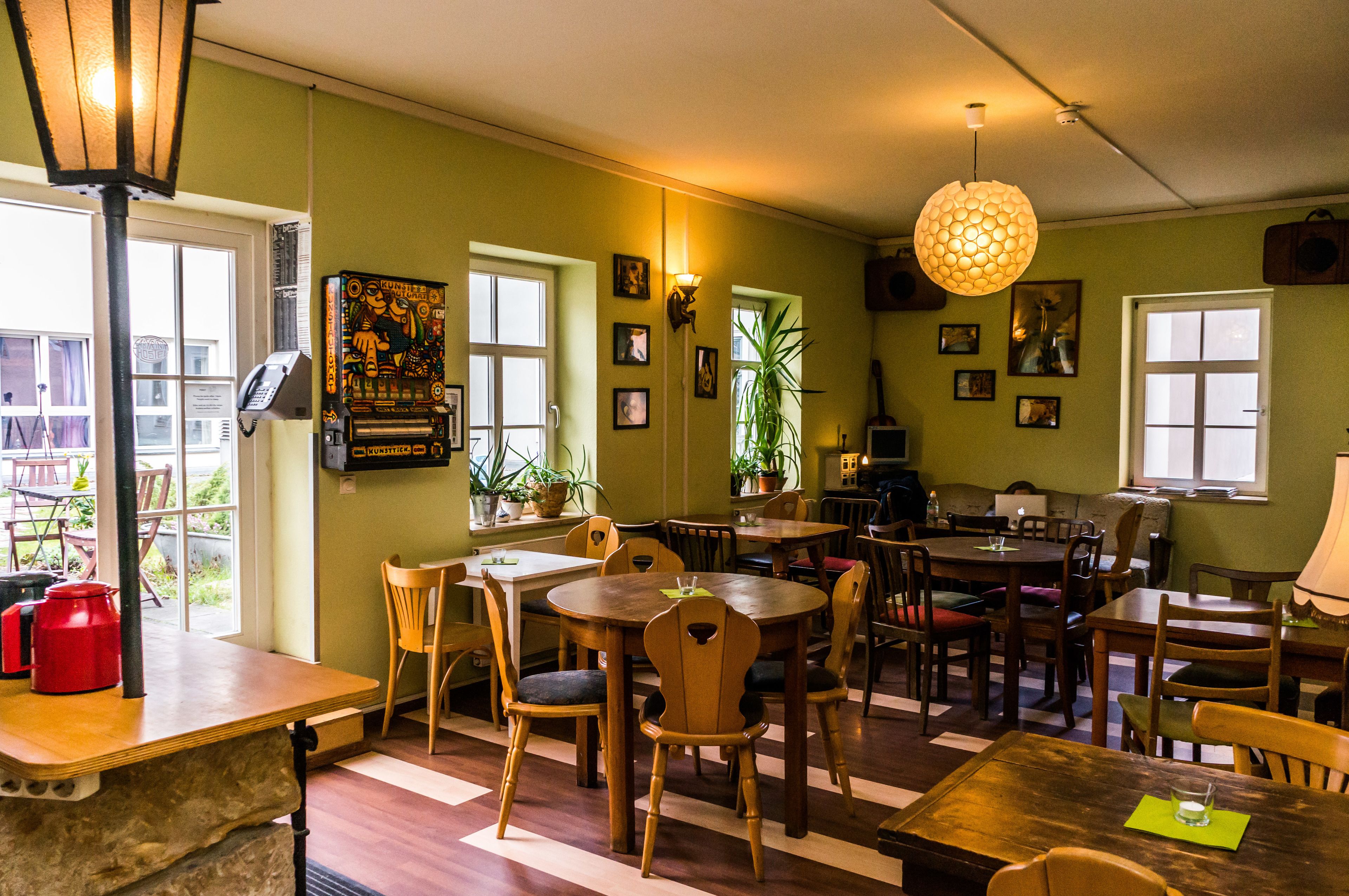 A cozy restaurant with wooden tables and chairs, potted plants, and artwork on the walls.