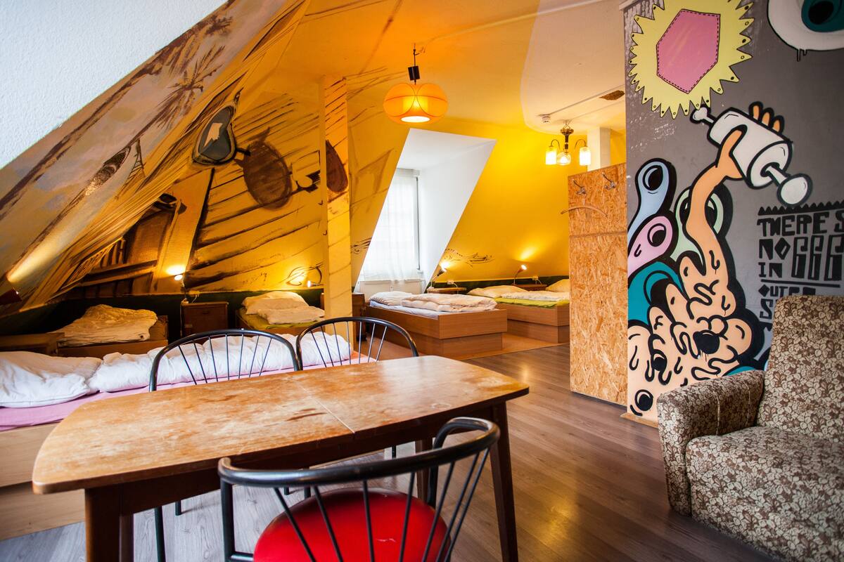 A cozy attic bedroom with a sloped ceiling, a wooden dining table, and a mural on the wall.