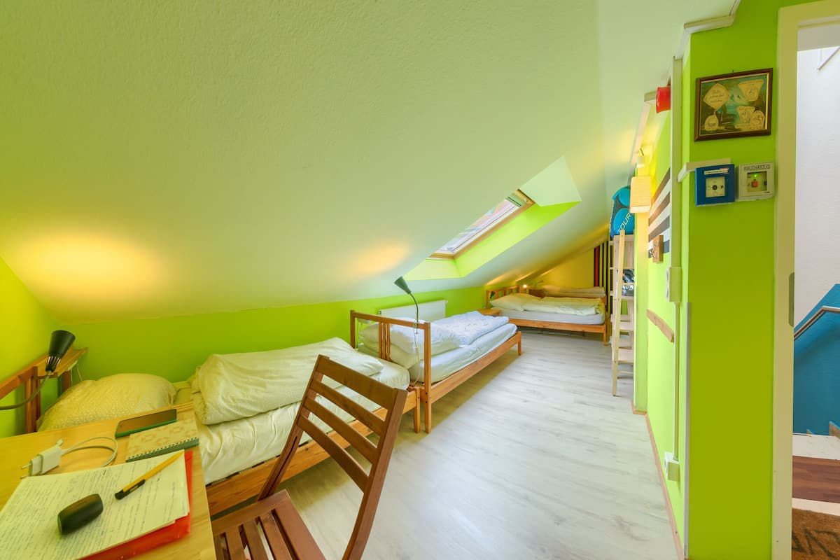 A small, brightly colored room with two wooden beds, a desk with a chair, and a skylight.