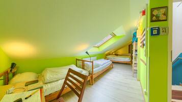Una habitación pequeña y luminosa, con dos camas de madera, un escritorio con silla y un tragaluz.