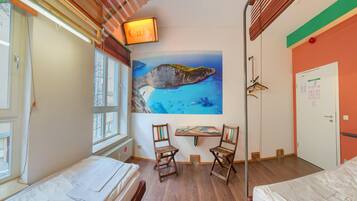 Habitación de hotel con dos camas, un escritorio y sillas, un cuadro de un paisaje costero y un cartel que dice 'Cafe'.
