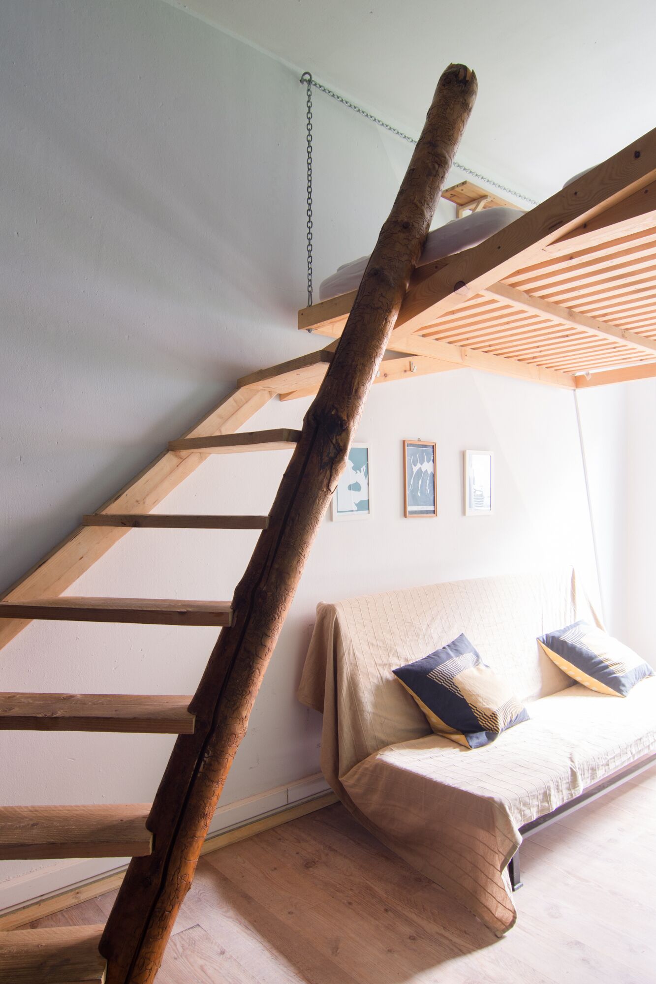 Ein Schlafzimmer im Loft-Stil mit einer Holzleiter, einem Bett mit Kissen und einem kleinen Tisch.