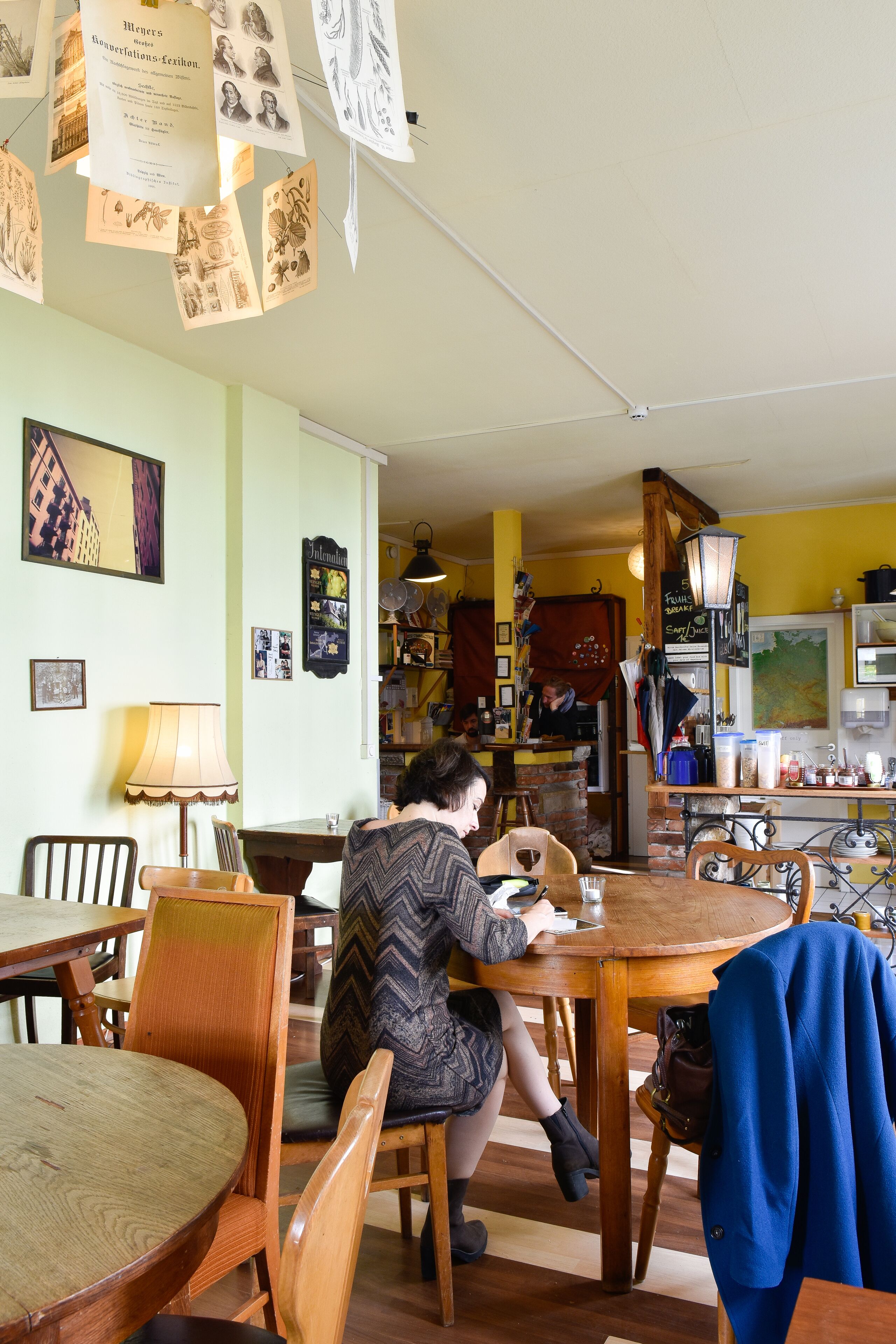 Un café acogedor con muebles de madera, una persona sentada en una mesa y varios papeles colgando del techo.