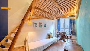 A cozy room with a wooden ladder, a white sofa, a wooden table, and a view of the street through large windows. - Labyrinth Hostel (Weimar)