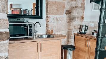 A kitchen with a stone wall, a microwave, a sink, and wooden cabinets.