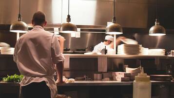 A chef in a professional kitchen with stainless steel counters, overhead lighting, and a focus on food preparation.