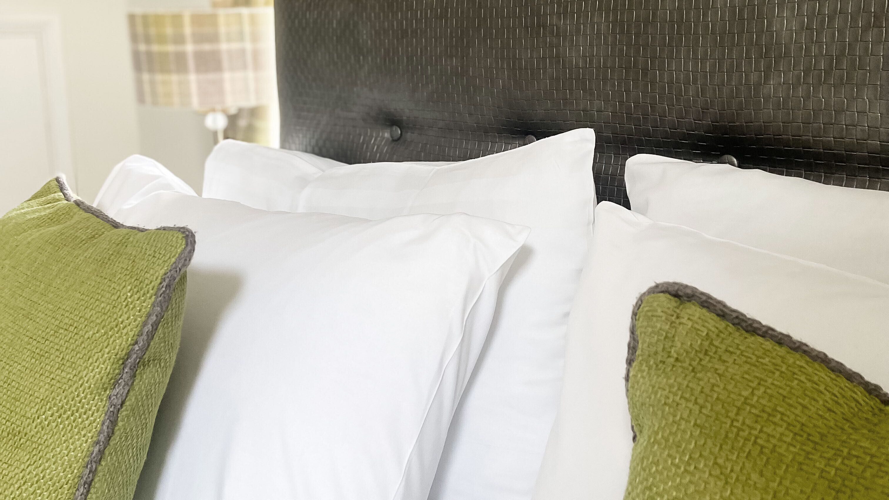 A bed with white and green pillows, a dark headboard, and a visible wall with a checkered pattern.