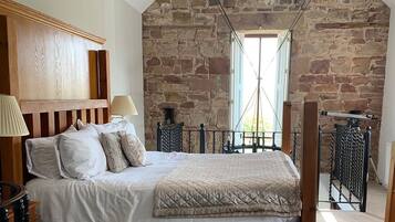 Een slaapkamer met een stenen muur, een houten hoofdbord, een bed met wit beddengoed en een balkon met een metalen hekwerk.