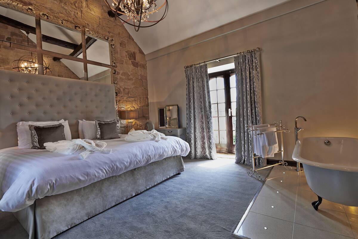 A spacious bedroom with a large bed, a classic clawfoot bathtub, and a stone accent wall.