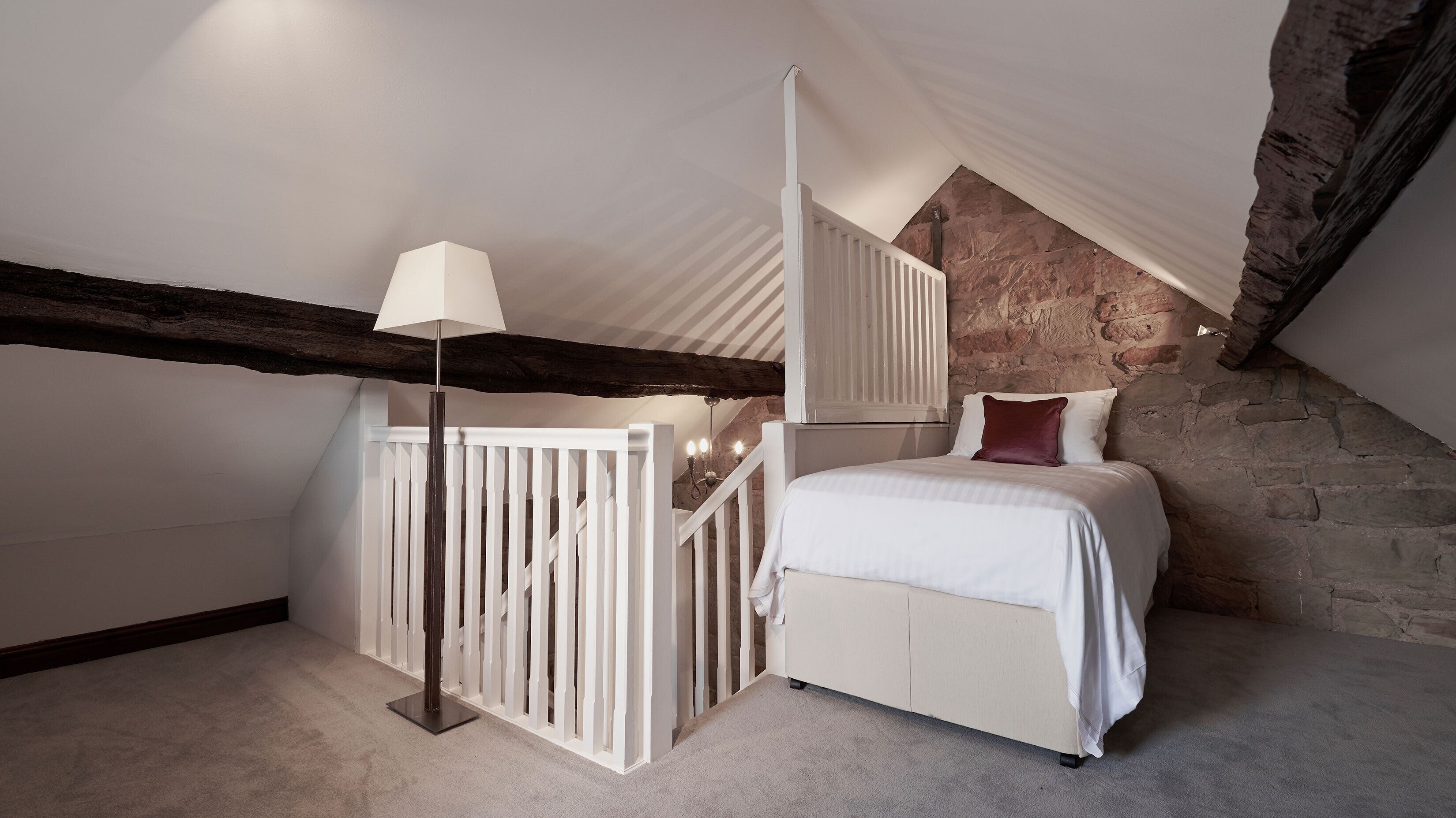 A bedroom with a white bed, a floor lamp, and a stone wall.