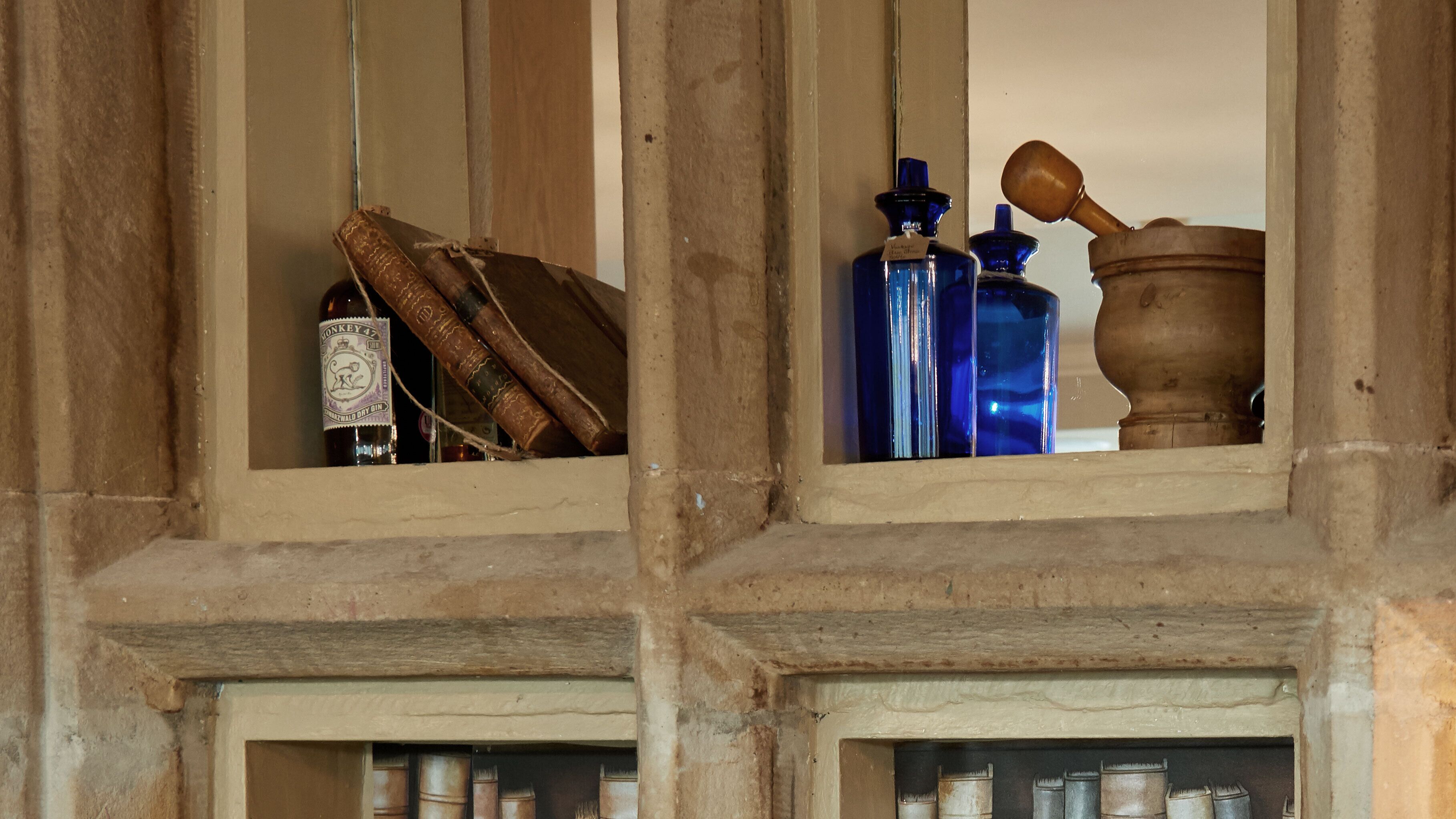 A window with a view of a room containing a wooden cabinet with bottles and a wooden object.
